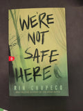 A book titled 'We're Not Safe Here' by Rinn Chupeco, featuring a green and yellow-green cover with black handwritten-style text, photographed on a dark surface.