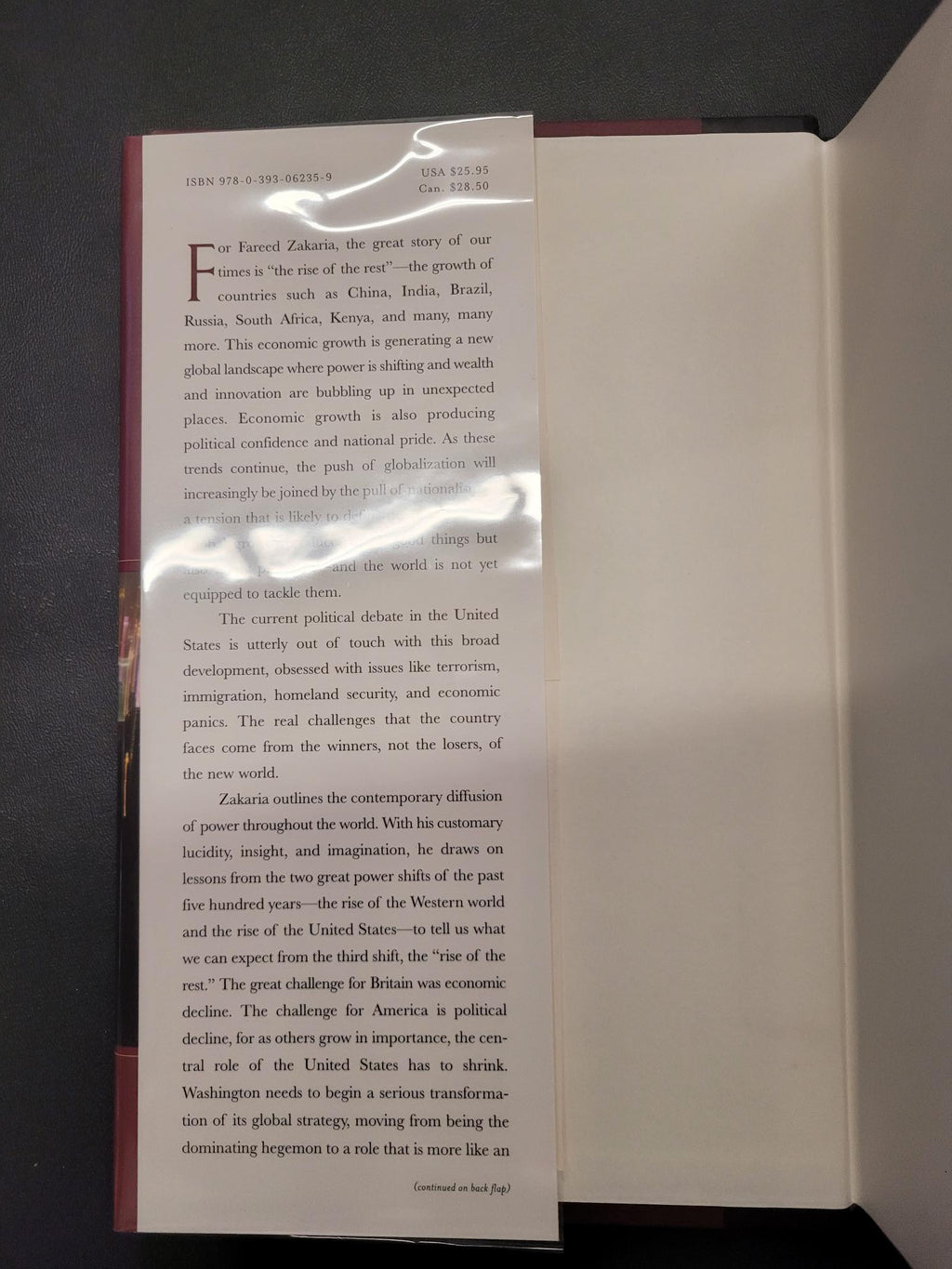 An open book or booklet showing printed text on a white page, photographed from above on a dark surface. A glossy plastic sleeve reflects light across the page.