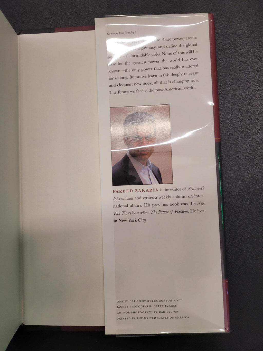 A book or booklet with printed text and a small inset photograph, photographed from above on a dark surface. The item appears to be a printed publication with a glossy cover or protective sleeve.