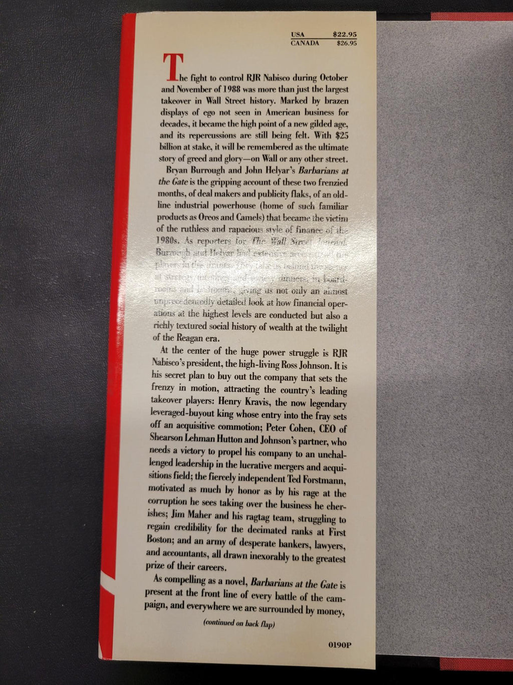 A printed book page or booklet page with dense black text on a cream paper background, photographed from above on a dark gray surface. A red border is visible along the bottom edge of the page.