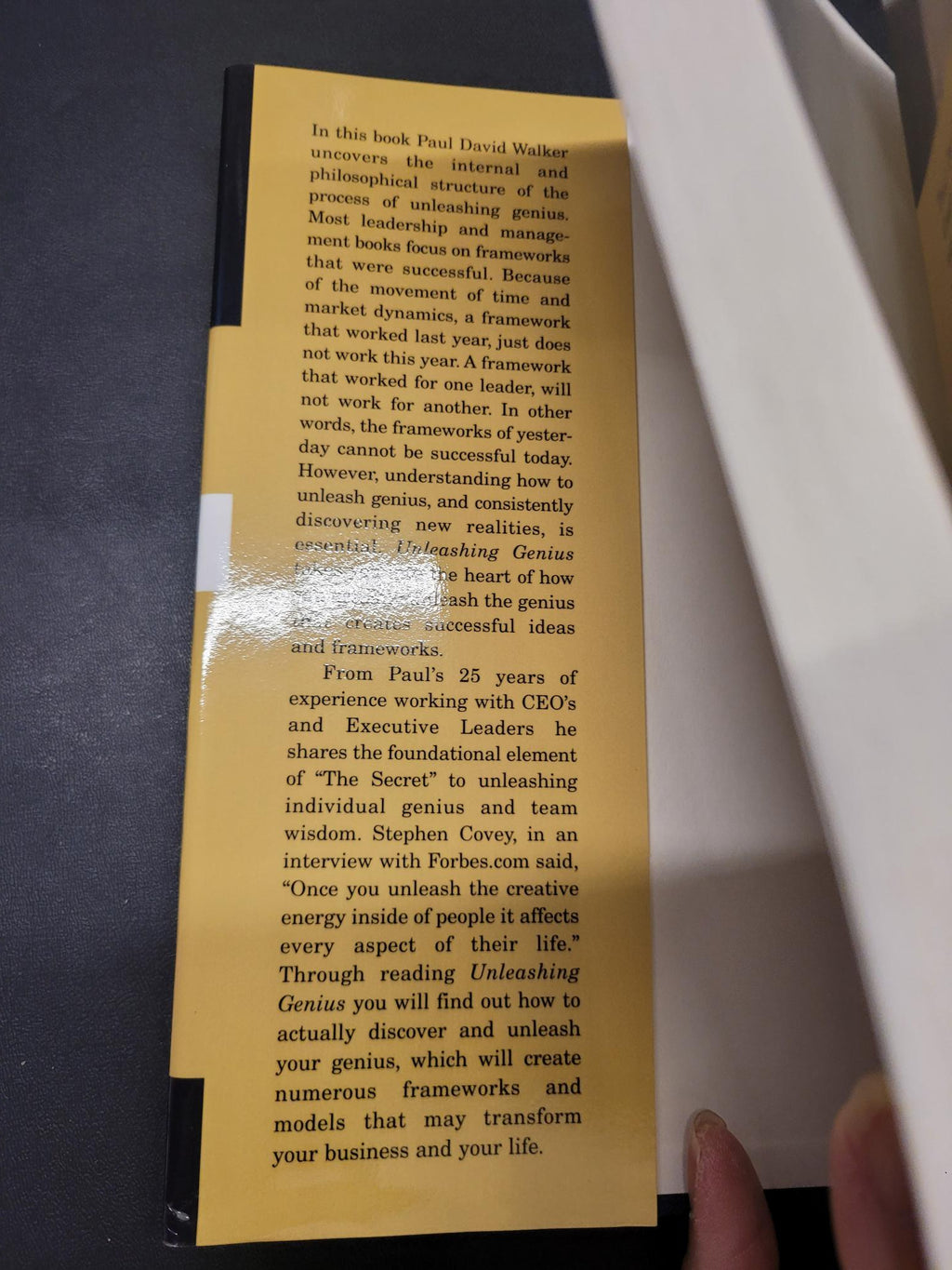 A close-up of a yellow rectangular printed card or bookmark with black text, held by a hand over a dark surface.