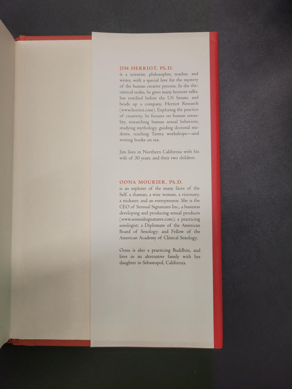 An open book or booklet showing printed text on a white page with a red top border, photographed from above on a dark gray surface.