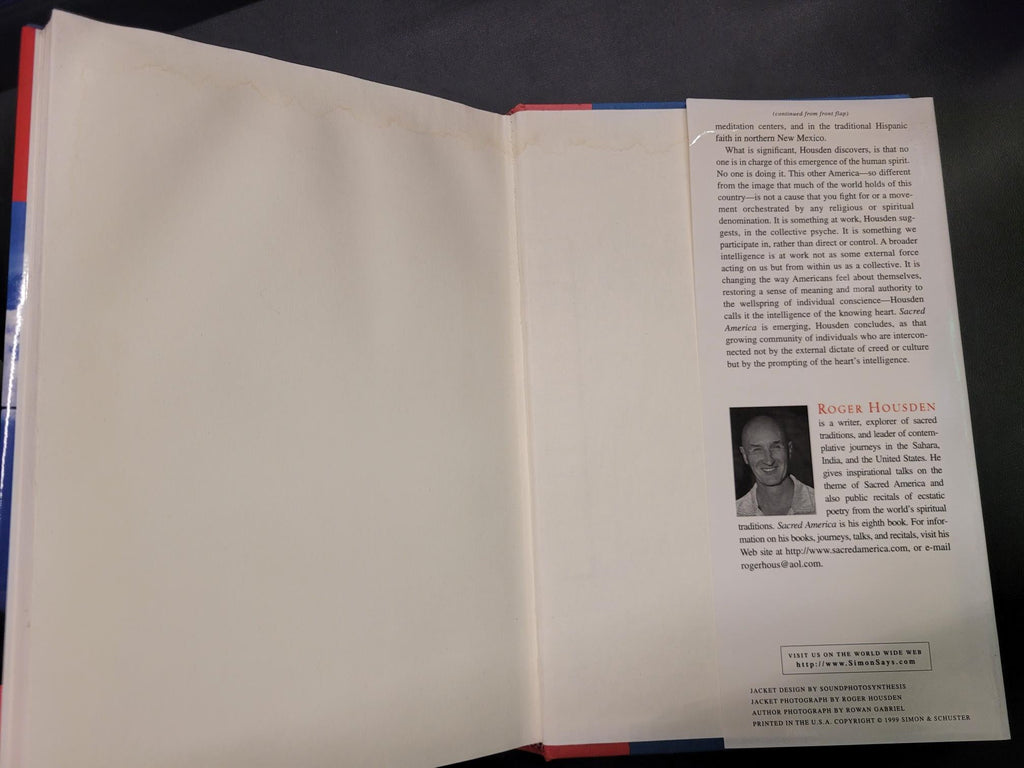 An open book or booklet showing blank cream-colored pages on the upper half and a printed insert page with text and a small portrait photo on the lower half, photographed against a dark background.
