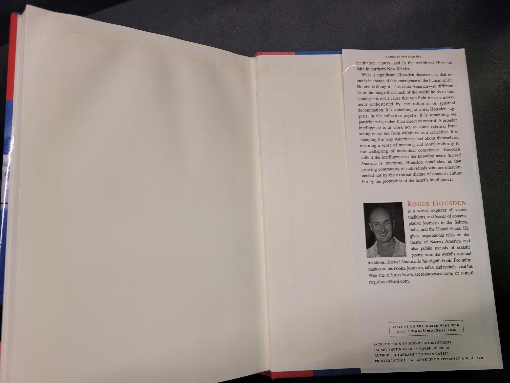 An open book or booklet showing blank cream-colored pages on the upper half and a printed insert page with text and a small portrait photo on the lower half, photographed against a dark background.