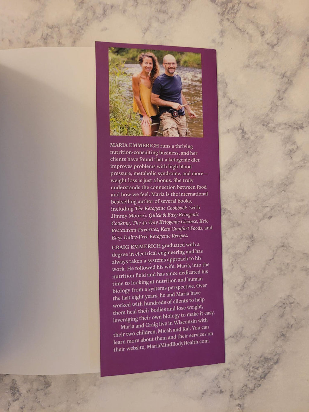 A purple printed card or booklet page with a small photo of two people outdoors and blocks of text, placed on a white sheet over a gray-and-white marble surface.