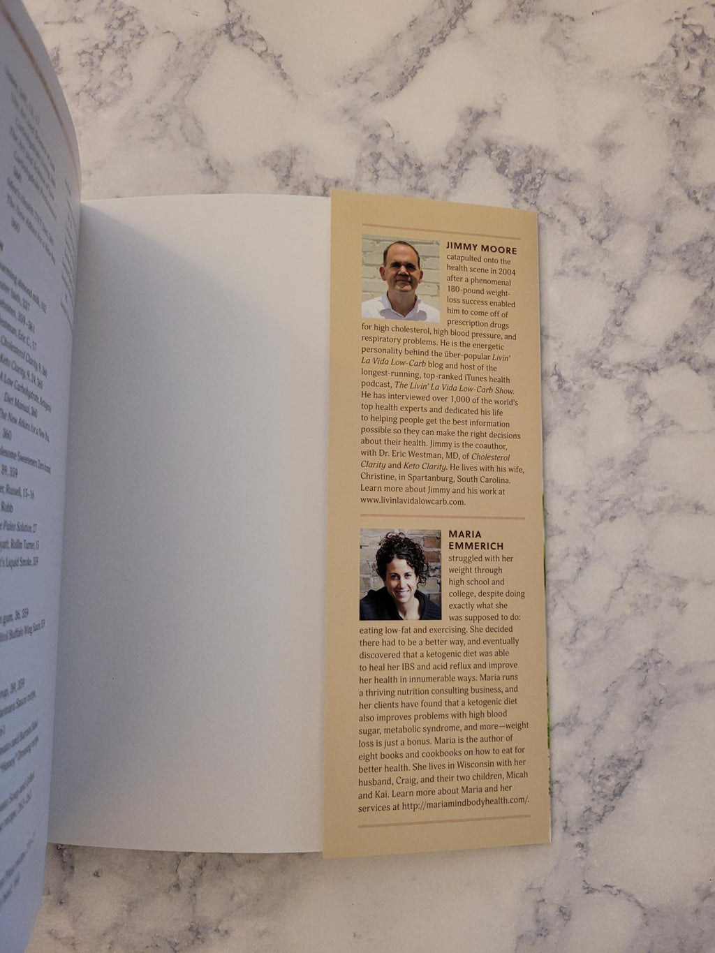 An open book or booklet laid on a white marble surface, showing a printed page with two small portrait photos and blocks of text. The product itself is not clearly identifiable beyond the printed booklet pages.