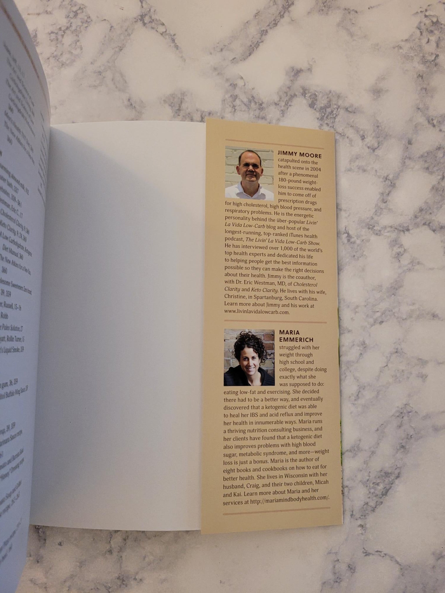 An open book or booklet laid on a white marble surface, showing a printed page with two small portrait photos and blocks of text. The product itself is not clearly identifiable beyond the printed booklet pages.