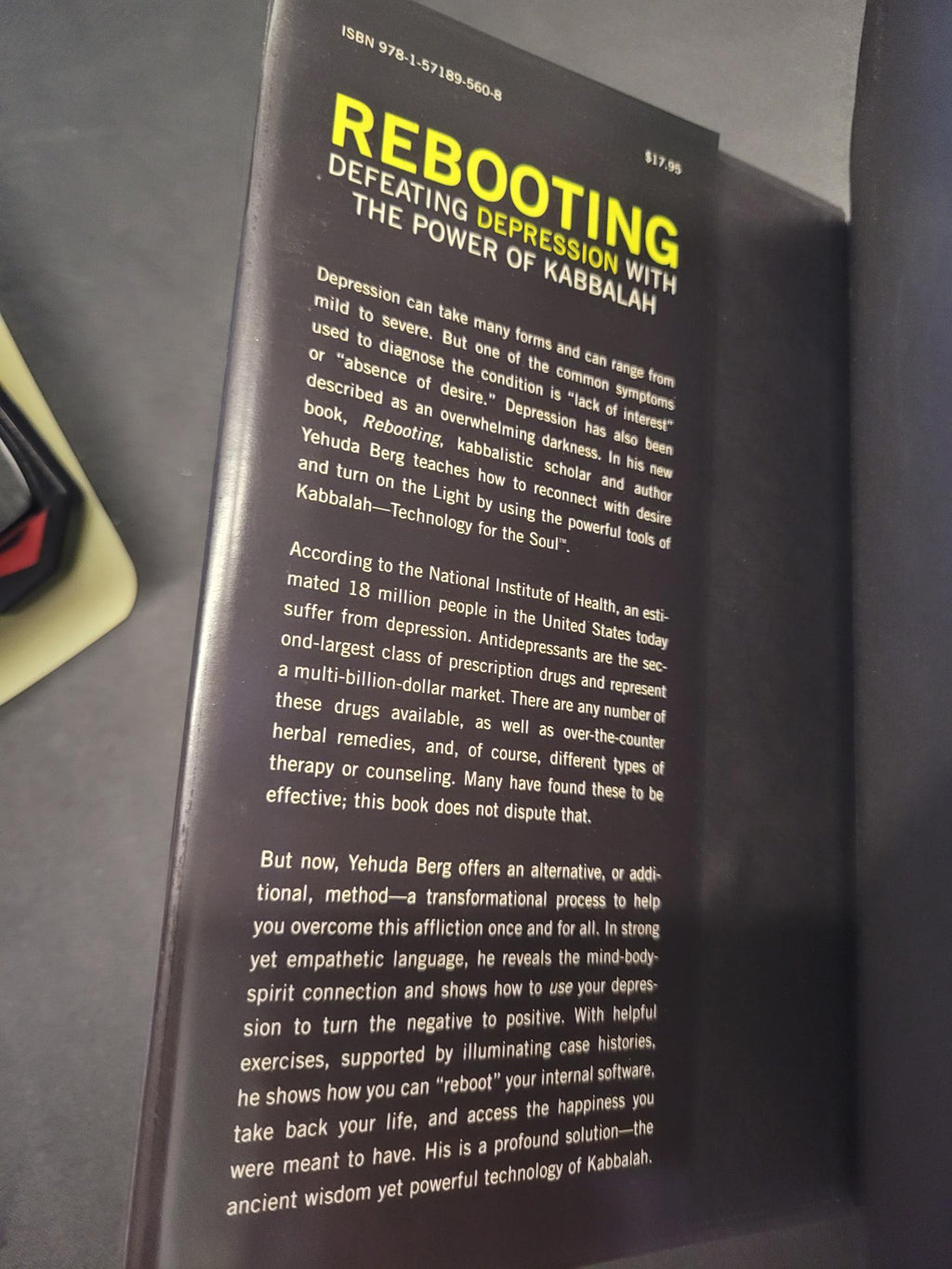 A close-up of a book or booklet cover titled 'REBOOTING' with large yellow text and dense white body text on a dark background, photographed on a gray surface.