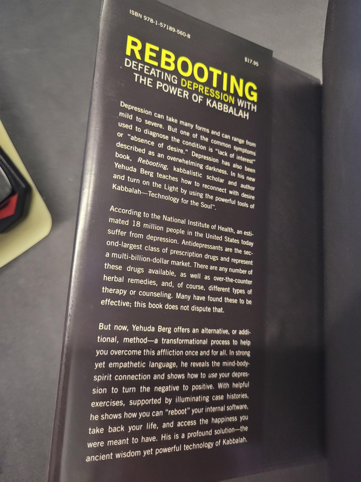 A close-up of a book or booklet cover titled 'REBOOTING' with large yellow text and dense white body text on a dark background, photographed on a gray surface.