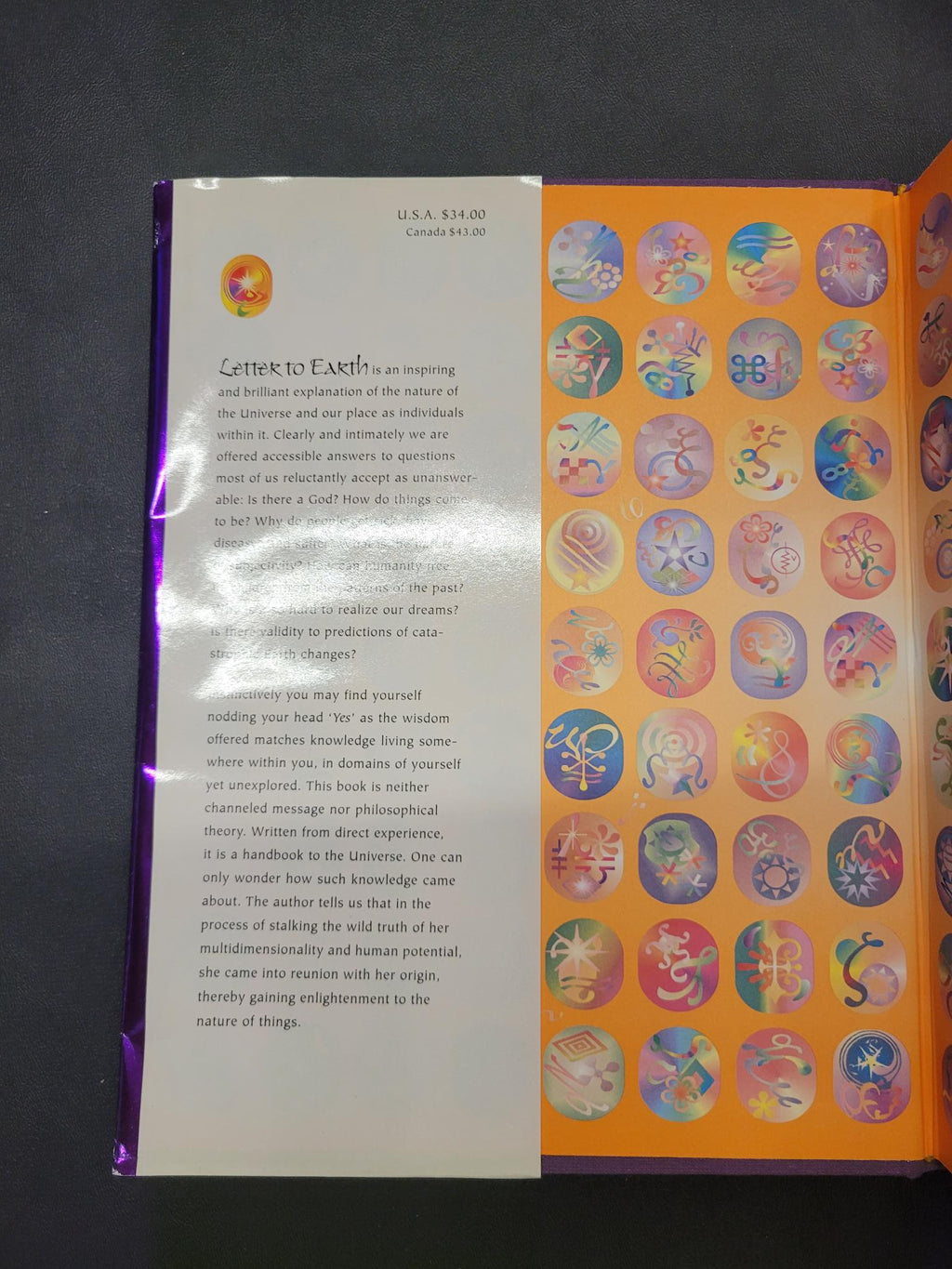 An open book or booklet with a bright orange cover featuring rows of colorful circular illustrations, and a white interior page with text, photographed on a dark surface.