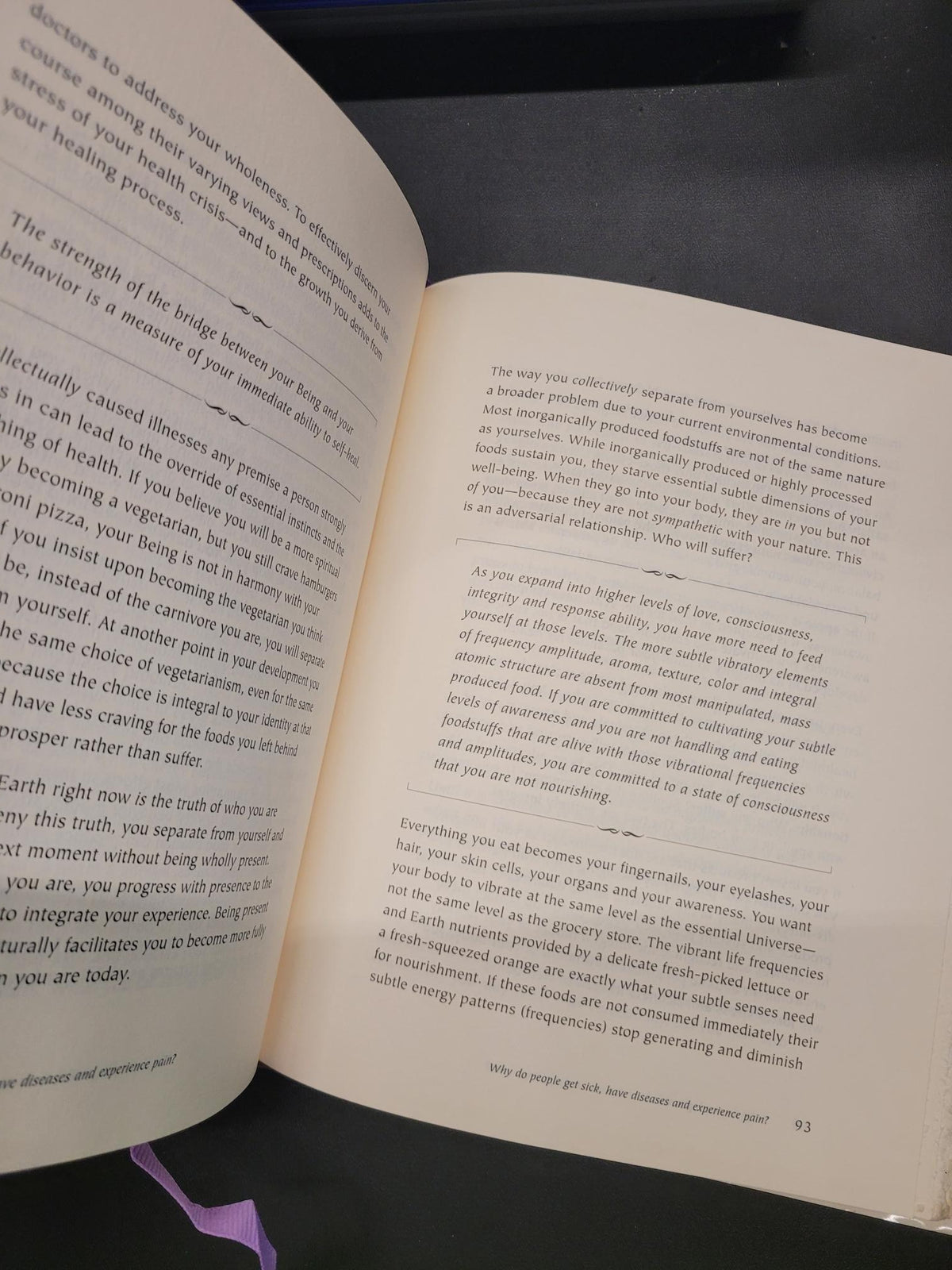 An open book showing printed text on cream-colored pages, photographed against a dark background with a small purple ribbon visible at the bottom right.