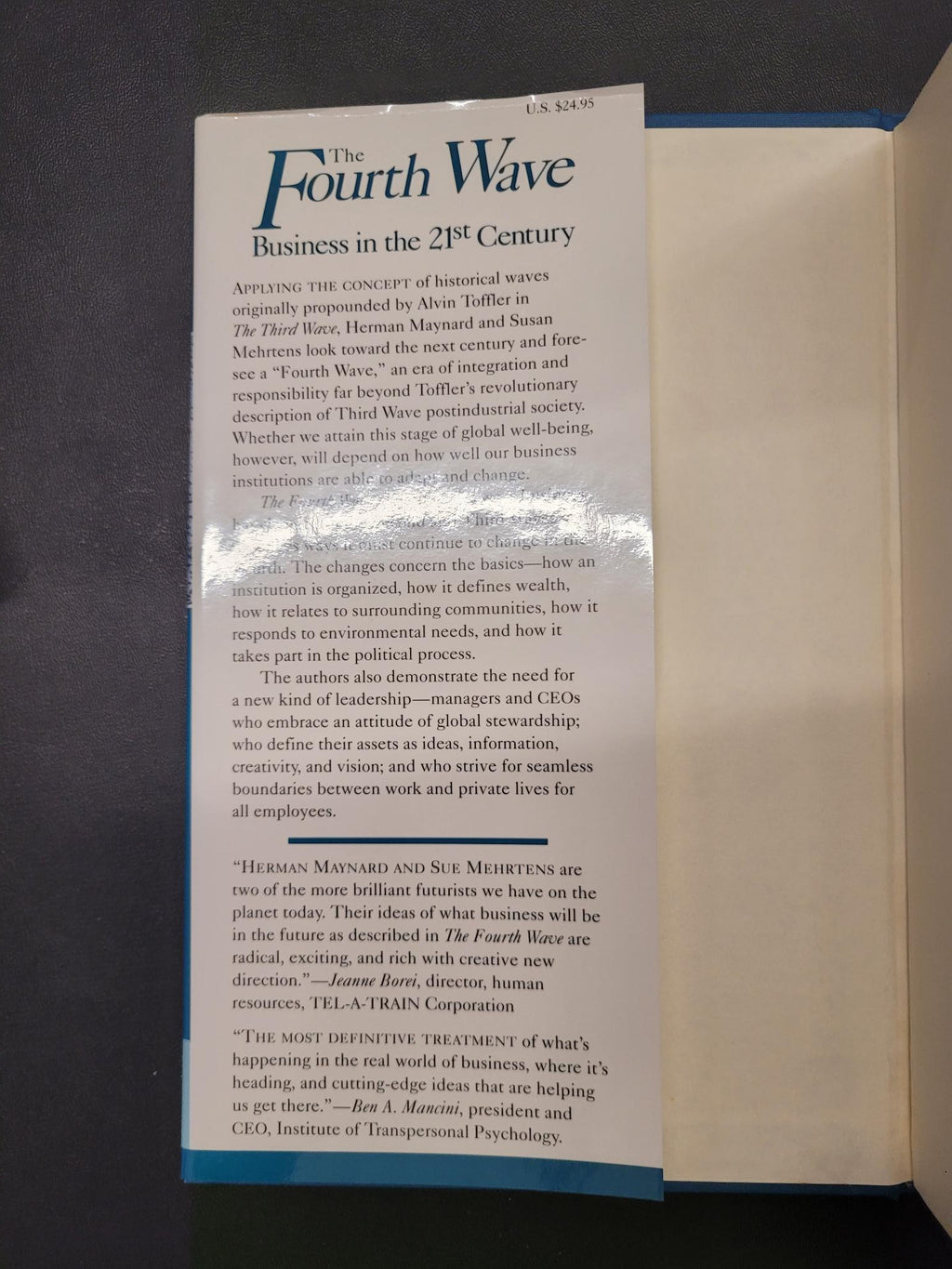 An open book or booklet lying on a dark surface, showing printed text pages with a prominent title reading 'The Fourth Wave' and a blue border along the page edges.