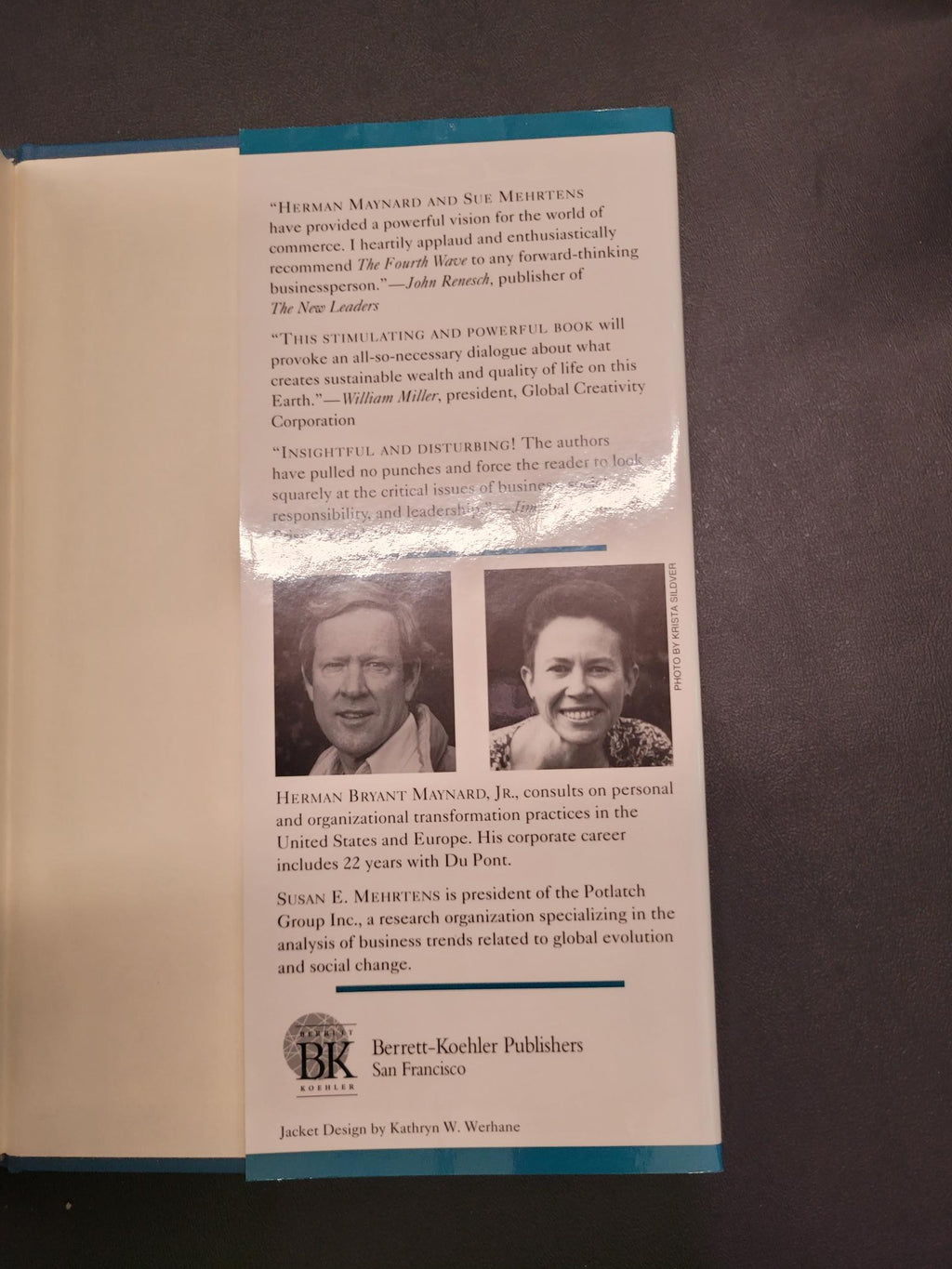 An open book or booklet lying on a dark surface, showing printed text, two small portrait photos, and a blue spine or cover edge. No person is present, but this is not a clean product hero shot; it appears to be an interior page view of a printed publication.
