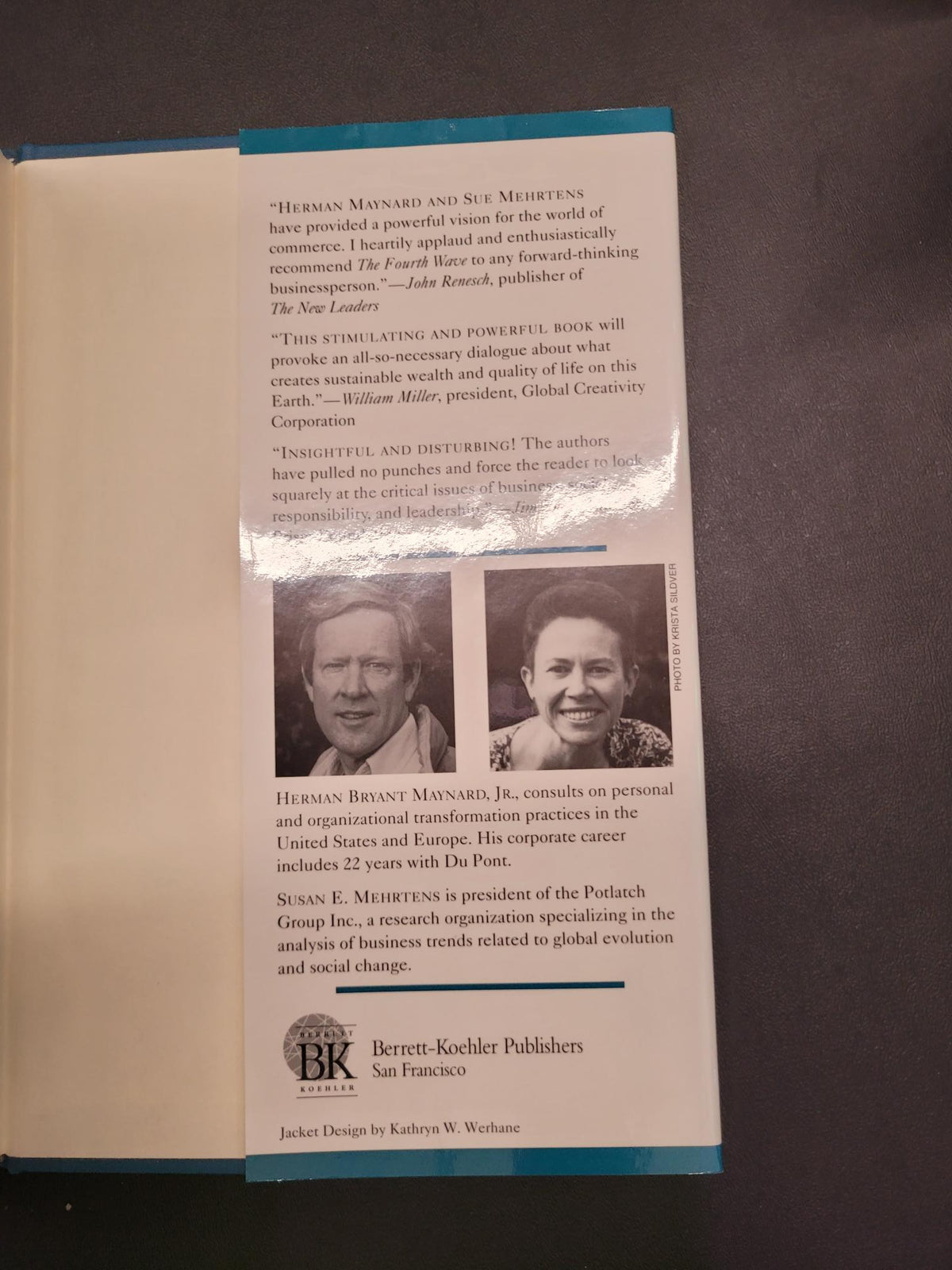 An open book or booklet lying on a dark surface, showing printed text, two small portrait photos, and a blue spine or cover edge. No person is present, but this is not a clean product hero shot; it appears to be an interior page view of a printed publication.