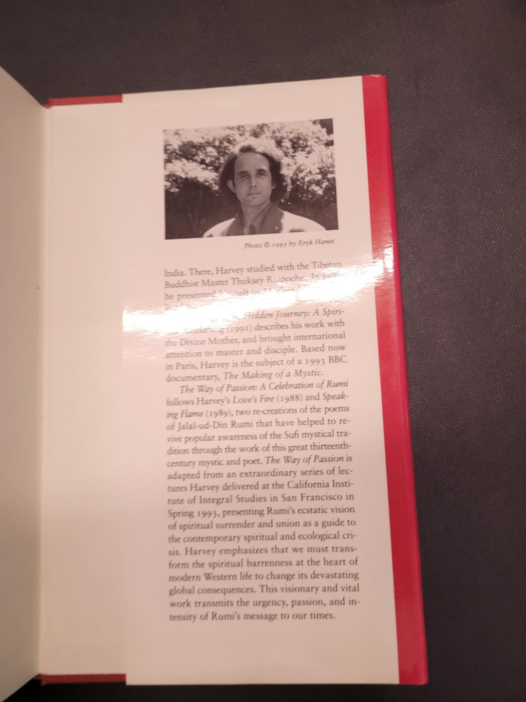 An open book or booklet showing a printed page with a black-and-white portrait photo, columns of text, and a red top border, photographed against a dark surface.