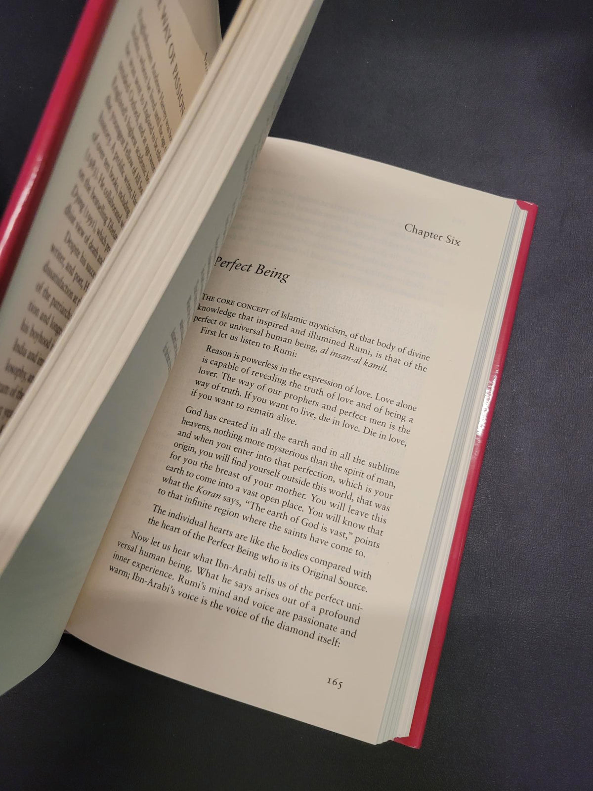 An open book with cream-colored pages and a red spine, photographed at an angle against a dark textured background.