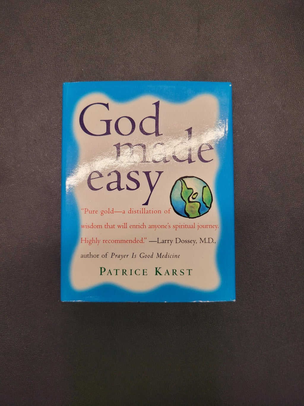 The book 'God Made Easy' by Patrice Karst, featuring a blue and beige cover with a small globe graphic, photographed on a dark textured background.
