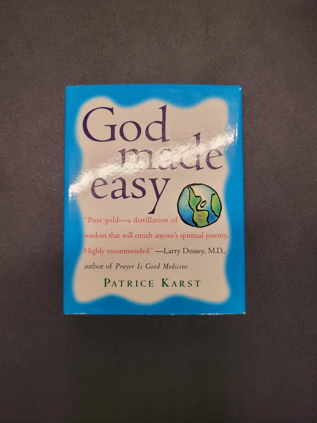 The book 'God Made Easy' by Patrice Karst, featuring a blue and beige cover with a small globe graphic, photographed on a dark textured background.