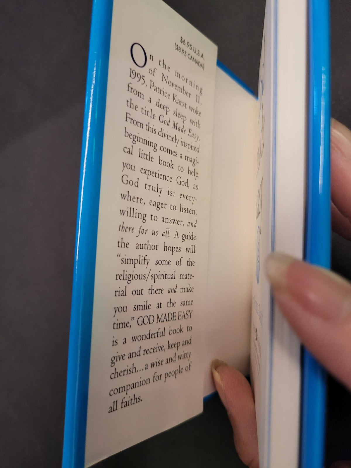 A close-up of a person's hands holding open a small book or booklet with a bright blue cover and cream-colored interior pages showing printed text.
