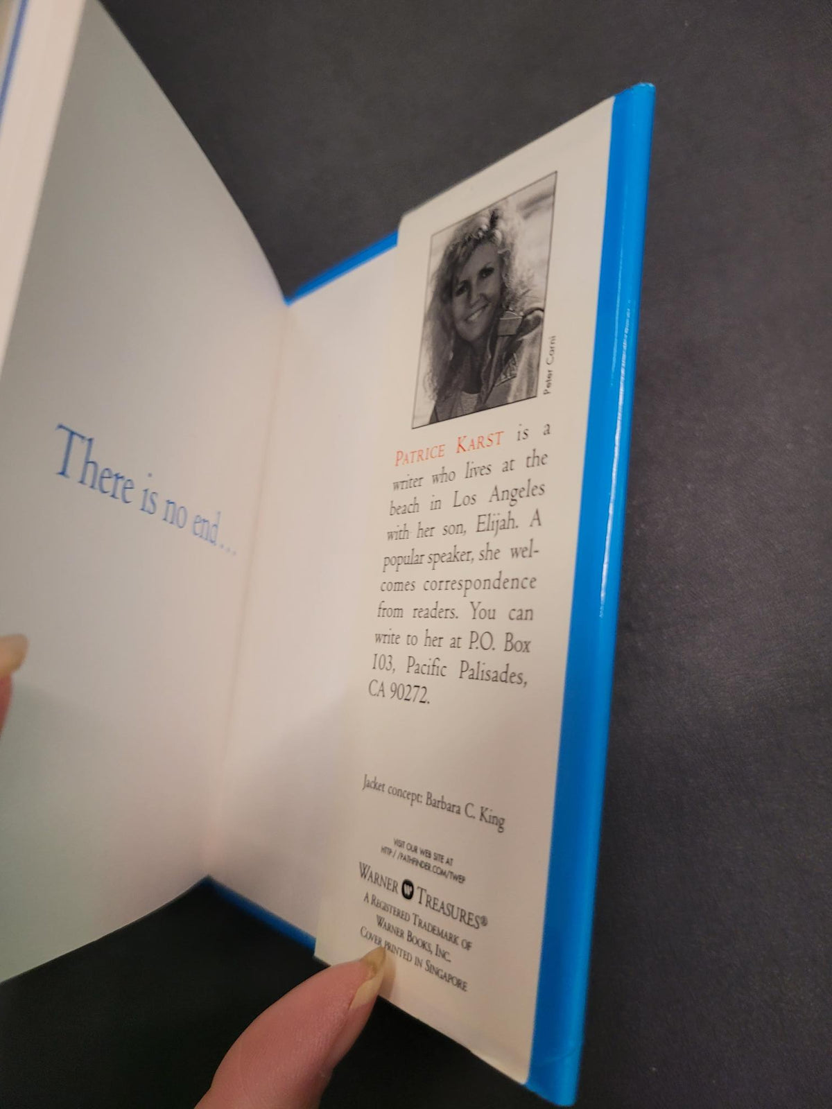 An open book or booklet with white pages and a bright blue cover edge, held by a person's fingers against a dark gray background. The left page contains a small black-and-white portrait, a red title, and text, while the right page has a blue heading and body text.