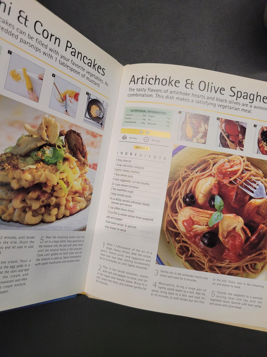 An open cookbook spread showing recipe pages with food photography, including a pasta dish and pancakes, photographed on a dark surface.