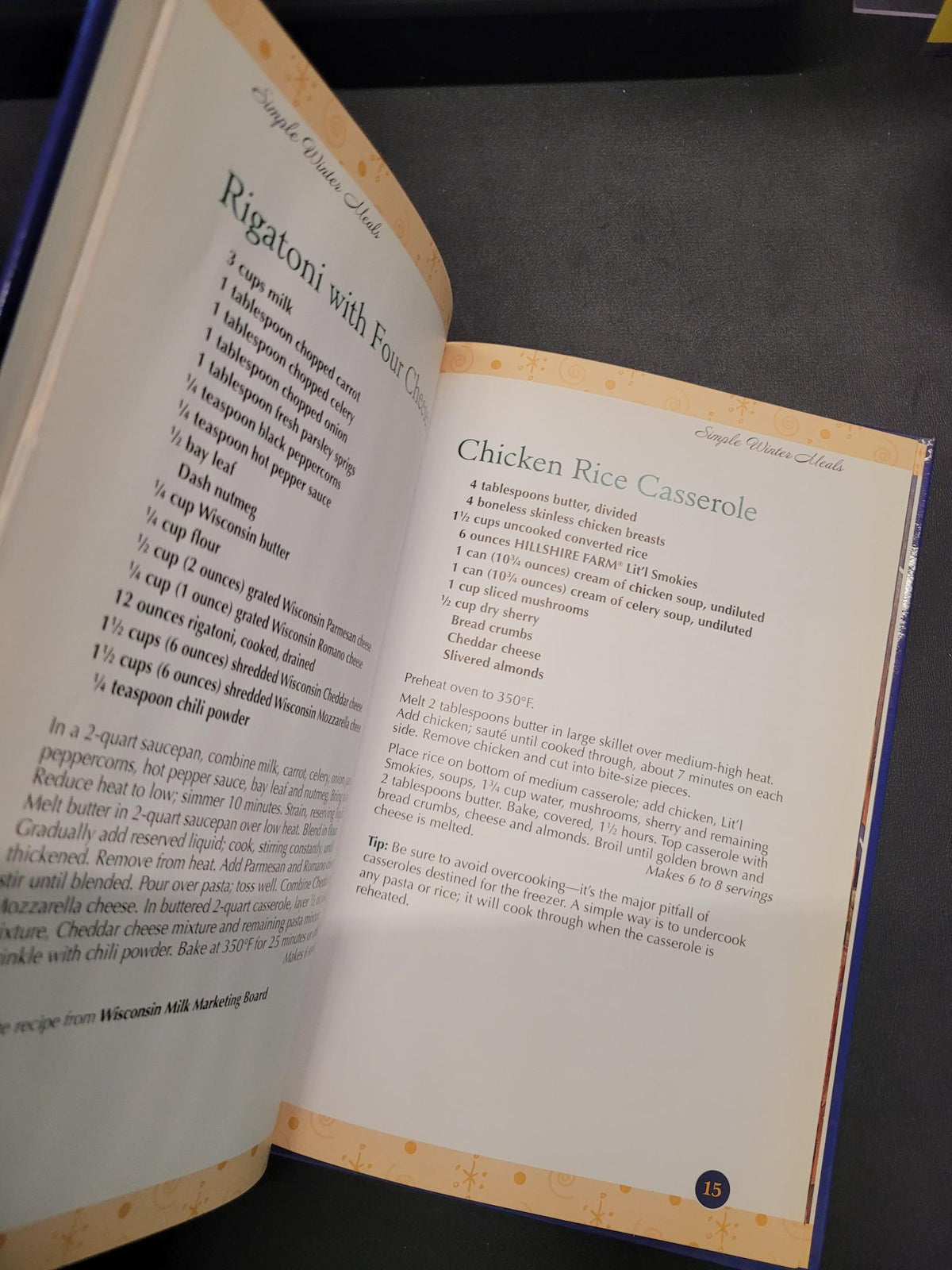An open cookbook showing two recipe pages, including Chicken Rice Casserole and Rigatoni with Four Peas, photographed against a dark background.