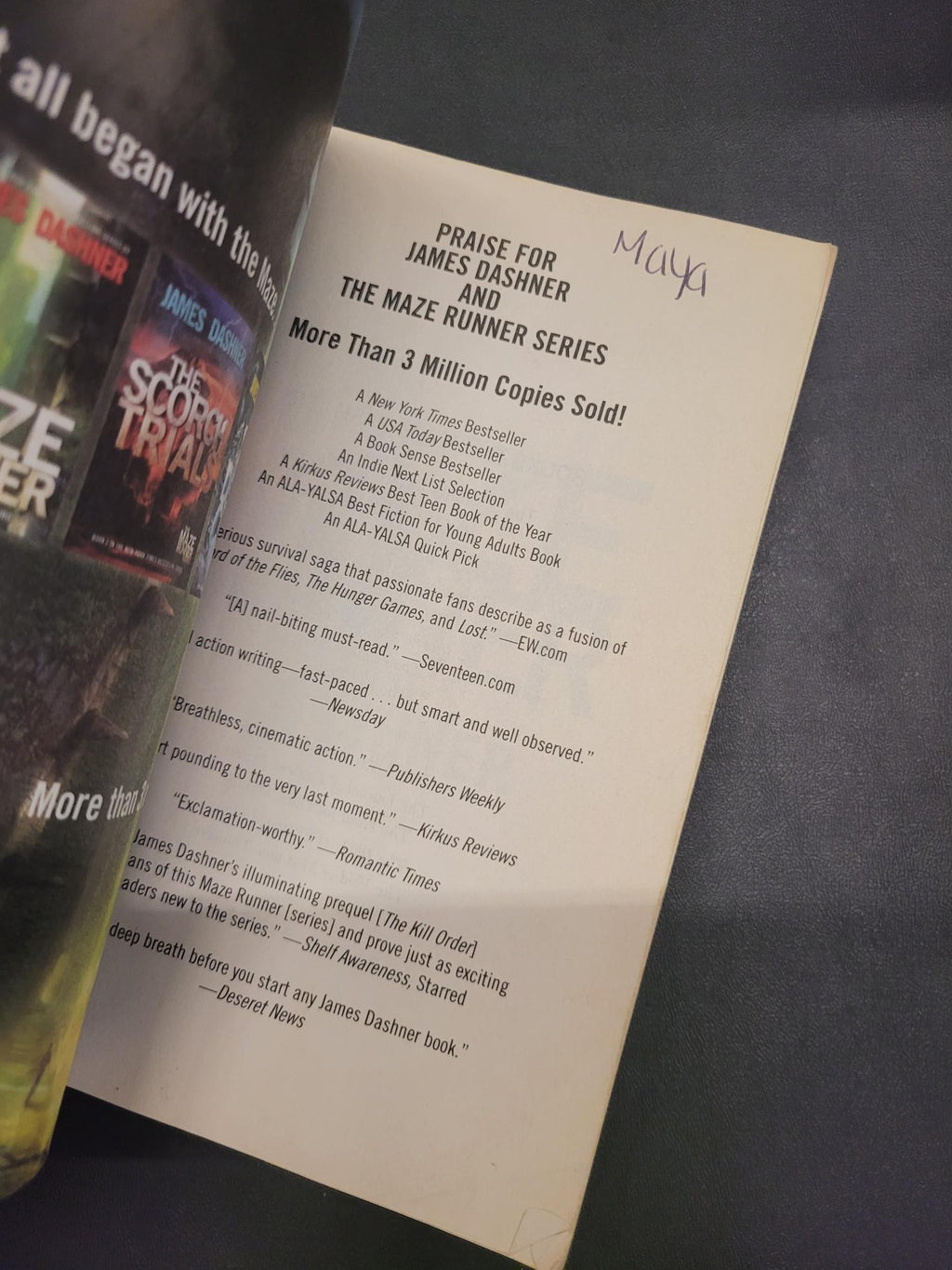 A close-up of a printed book review or author quote card for 'The Maze Runner Series' by James Dashner, placed over a book cover on a dark surface.