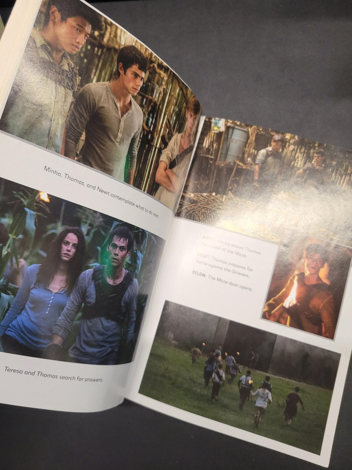 An open printed book or magazine spread photographed on a dark surface, showing multiple printed photos and text pages with no person physically present in the scene beyond the photographed object.