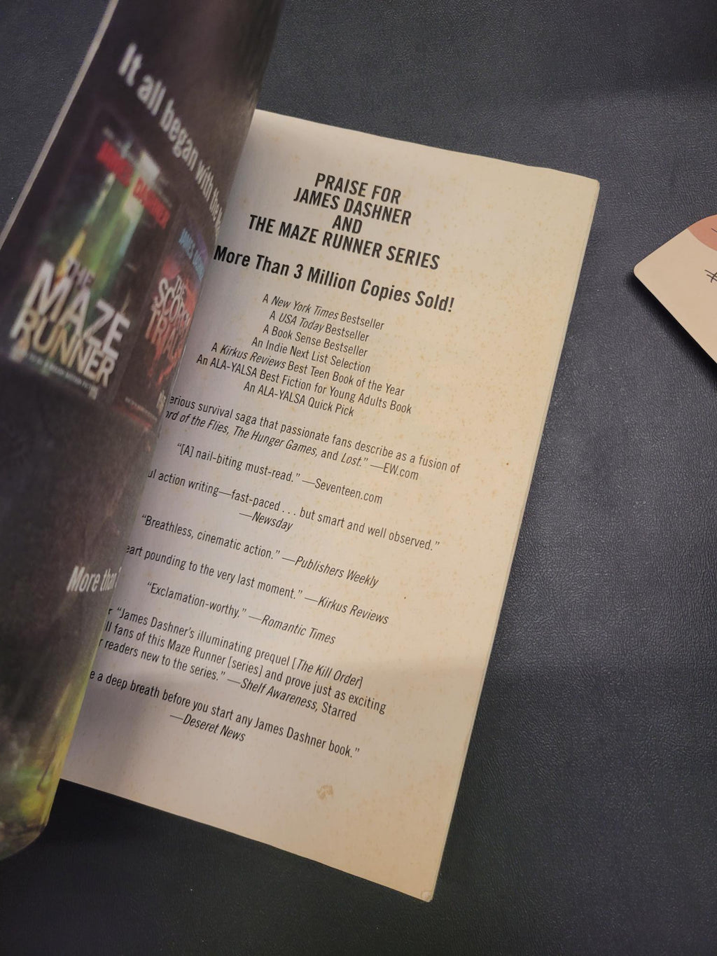 A printed book or booklet page with visible text and a partial cover design in the foreground, photographed on a dark blue fabric surface.