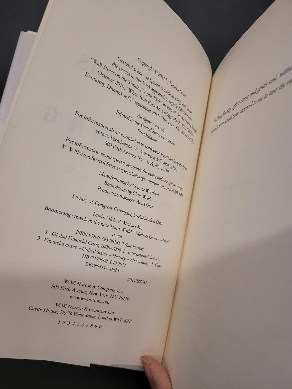 An open book showing printed text on the inner pages, photographed from above against a dark background. A person's fingers are visible holding the right page.