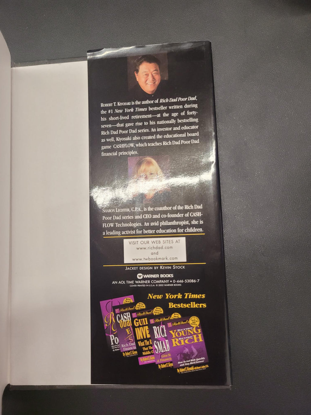 A glossy printed booklet or program cover photographed from above on a dark gray surface. The booklet has a black background with white text, small portrait photos, and a prominent purple and yellow New York Times cover graphic on the right side.