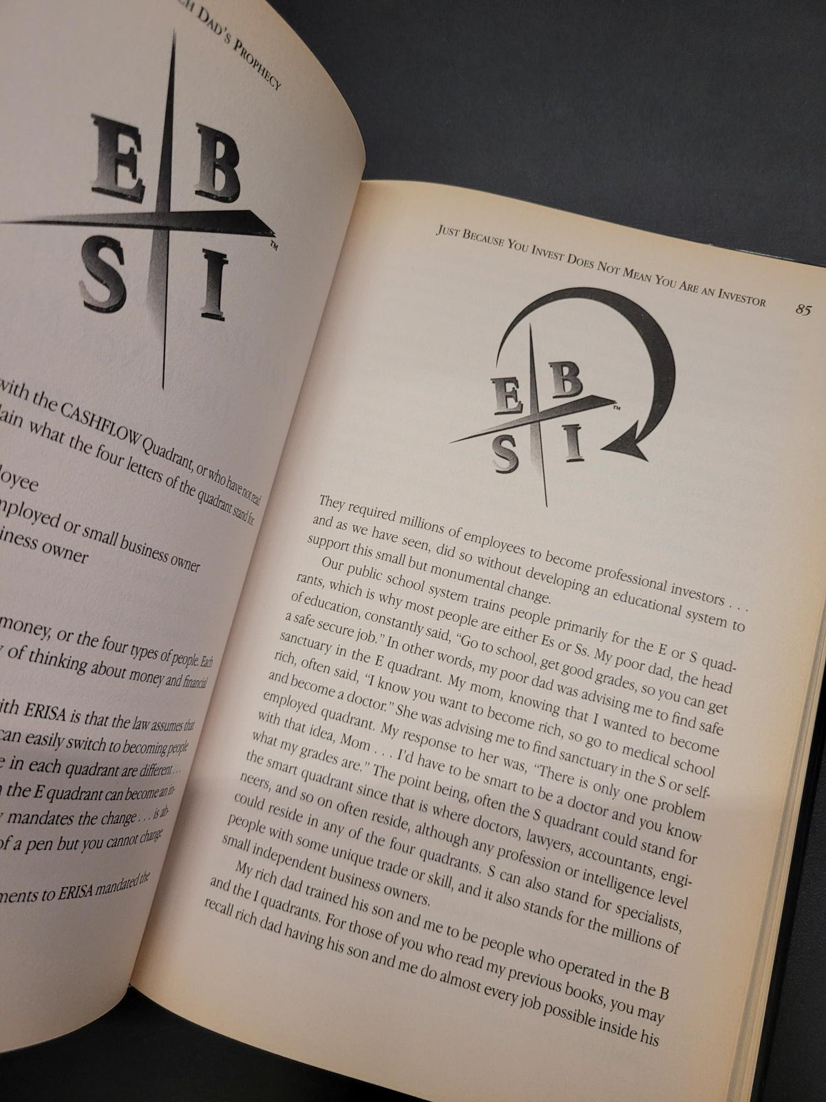 An open book showing printed text and a large black EBST logo on both pages, photographed against a dark gray background.