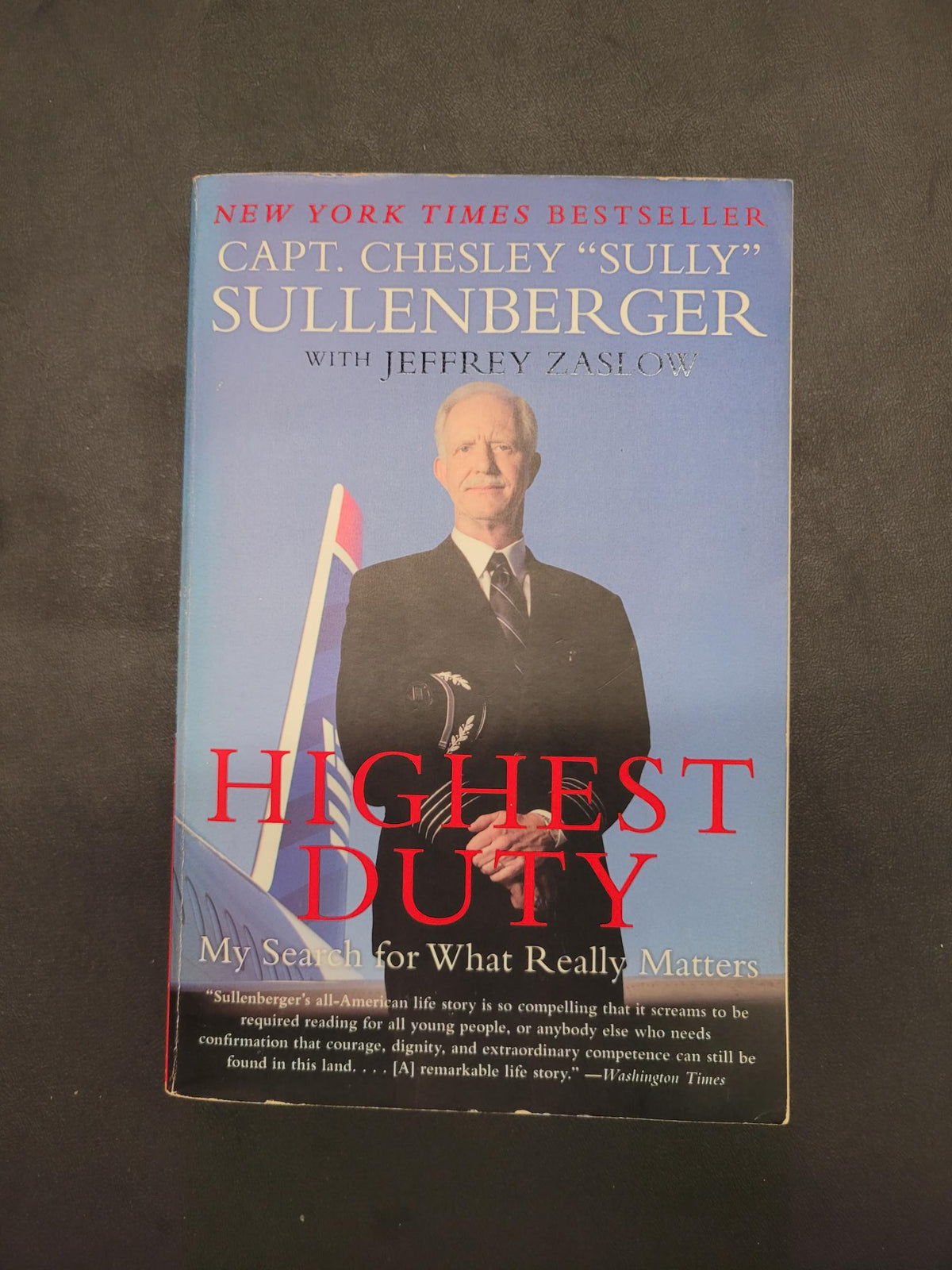 A paperback copy of the book 'Highest Duty: My Search for What Really Matters' by Capt. Chesley 'Sully' Sullenberger with Jeffrey Zaki, featuring a portrait of Sullenberger on the front cover against a dark gray background.