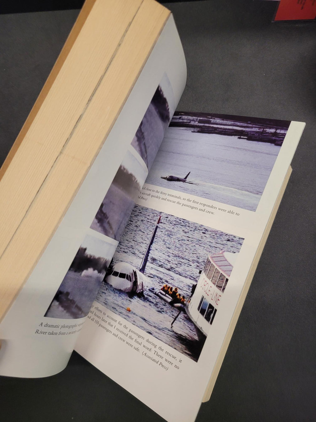 An open book showing printed pages with black-and-white and muted color photographs, photographed against a dark gray background.