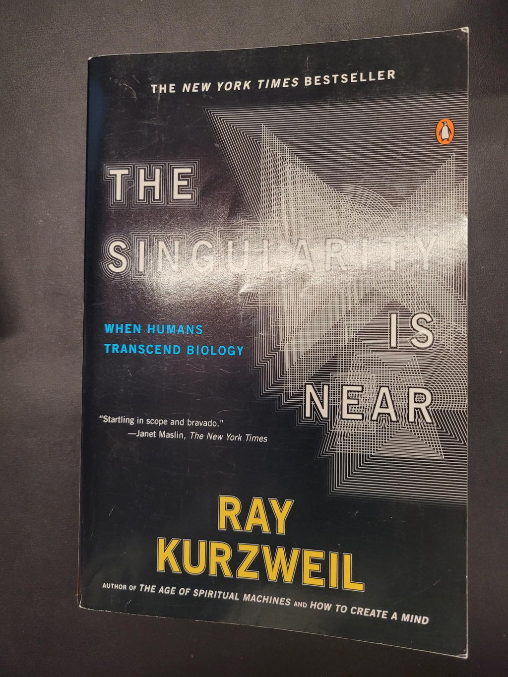 The front cover of the book 'The Singularity Is Near' by Ray Kurzweil, published by Penguin. The cover is predominantly black with a gray geometric pattern, white text, and yellow author name.