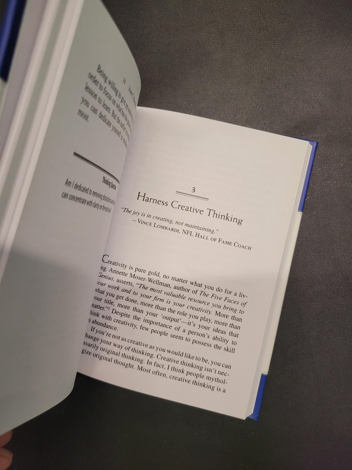 An open book showing printed pages with the heading 'Harness Creative Thinking' and body text, photographed against a dark gray surface.