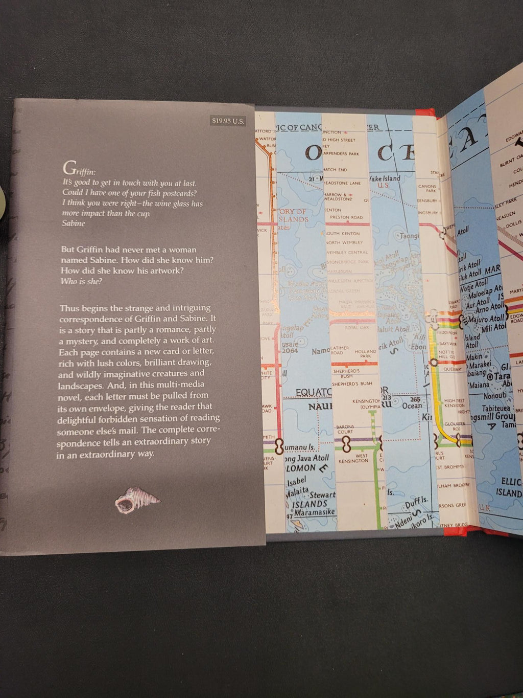 An open book or booklet showing a map spread on one page and a dark gray text page with white lettering on the other, photographed from above on a dark surface.