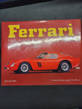A book titled "Ferrari: The Road From War" with a bright red cover, large yellow Ferrari logo, and a red sports car illustration, photographed on a dark surface.