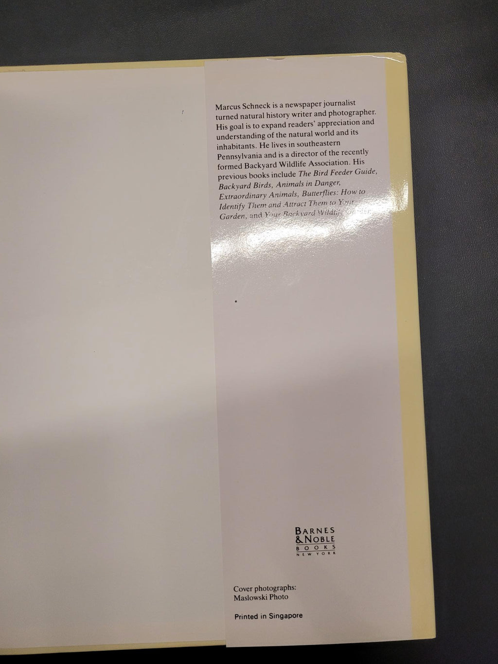 A cream-colored art print or book cover with black text, photographed from above on a dark gray surface. The cover features a light beige border and a glossy reflection in the center.