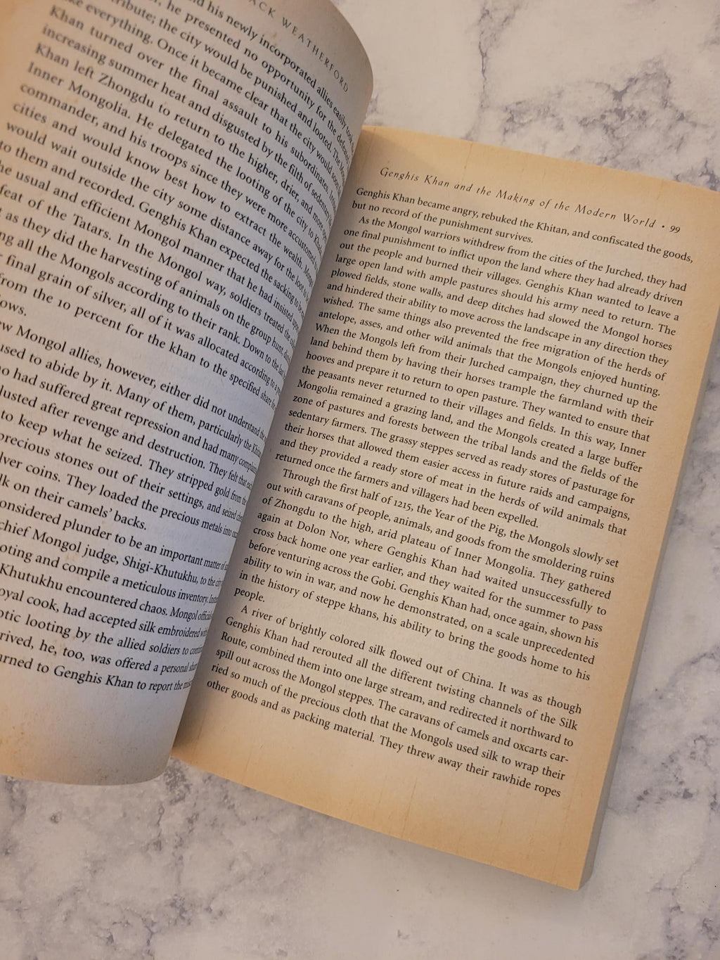 An open book showing printed text on its pages, placed on a light marble surface.