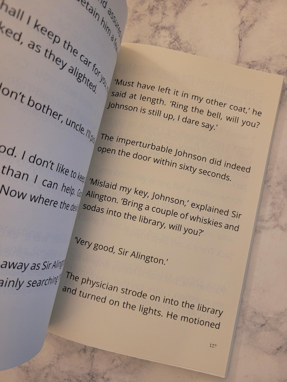 A close-up of an open book showing printed text on cream-colored pages, resting on a light marble-like surface.