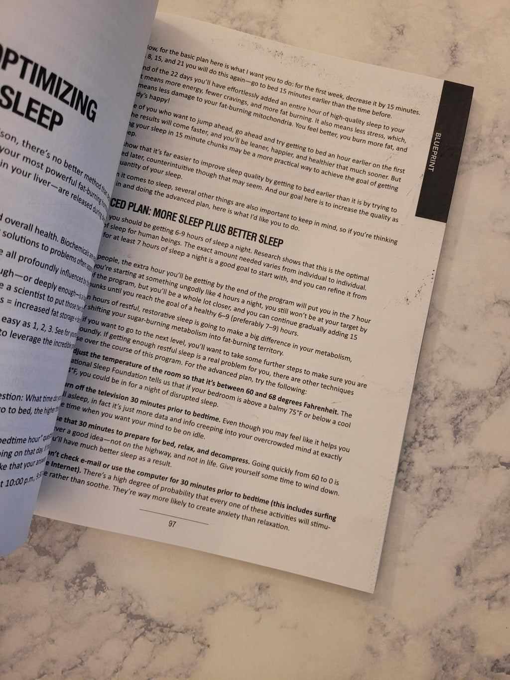 An open printed booklet or magazine page laid on a light marble surface, showing black text on white paper with a dark header at the top.