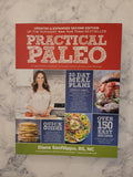 The front cover of the book 'Practical Paleo' by Diane Sanfilippo, BS, NC, displayed on a light gray and white marble surface. The cover features a prominent red top section with white textured title text, a central collage of photos and text blocks, and a green band at the bottom.