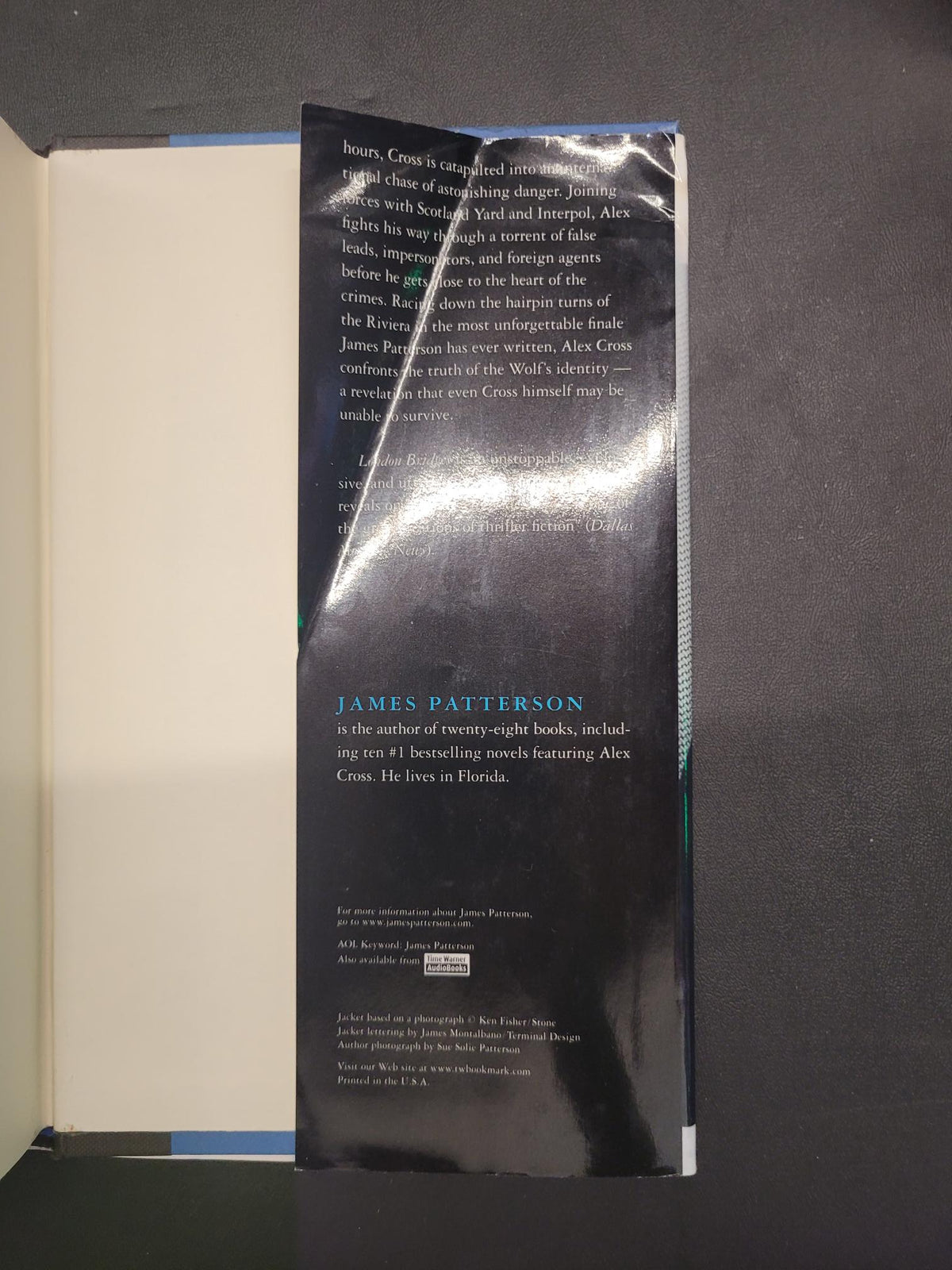 The back cover of a book, featuring a glossy black background with white and blue text, partially covered by a clear plastic protective sleeve, set against a dark gray background.
