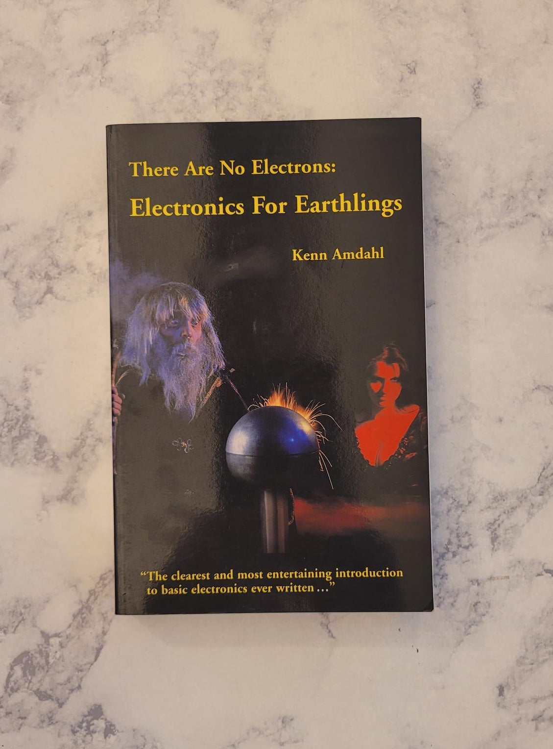 A paperback book titled 'There Are No Electrons: Electronics For Earthlings' by Kenn Andahl, lying flat on a white and gray marble-patterned surface.