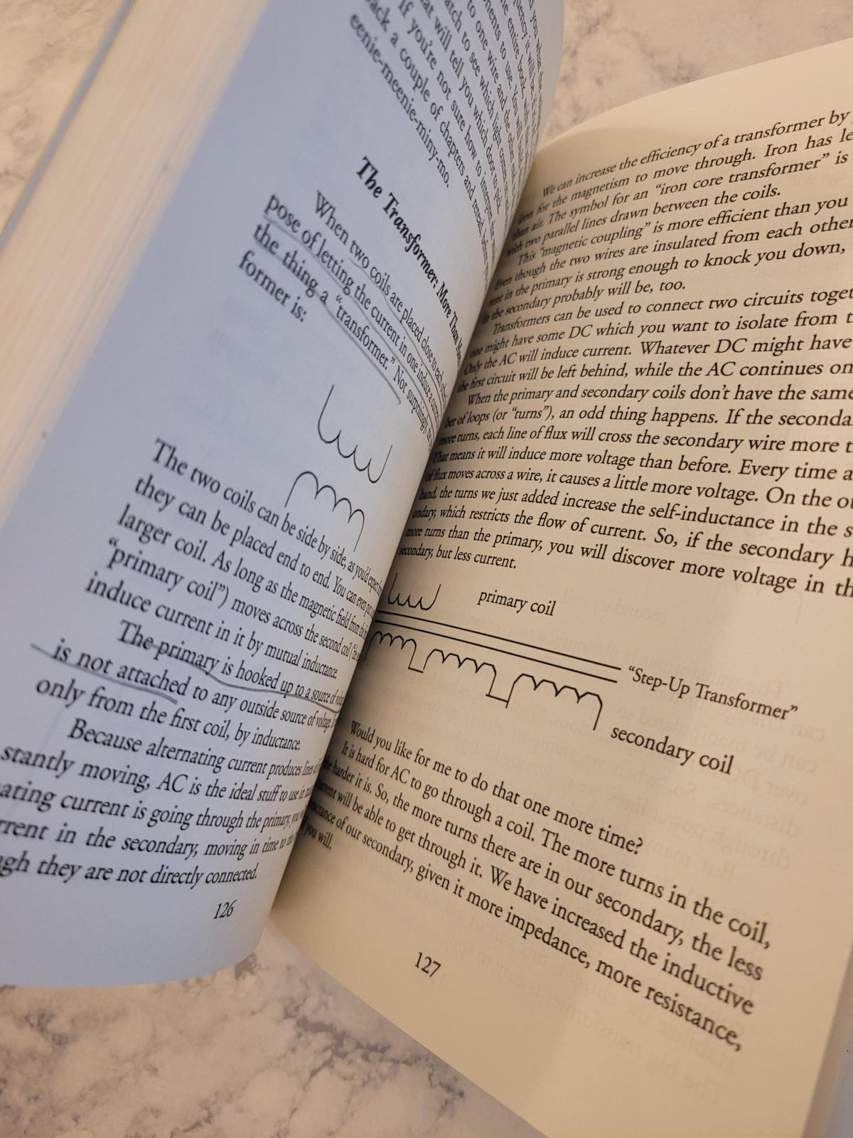 An open book spread on a light marble surface, showing printed text and handwritten signatures on both pages.