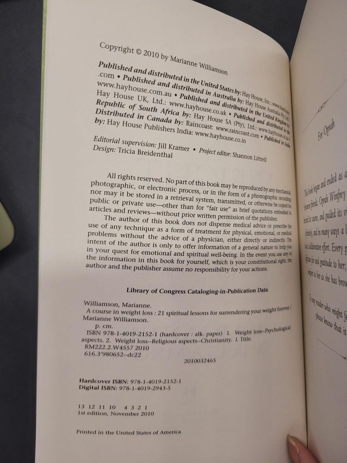 An open book showing printed text and copyright information on the left page, with a hand holding the right page against a dark background.