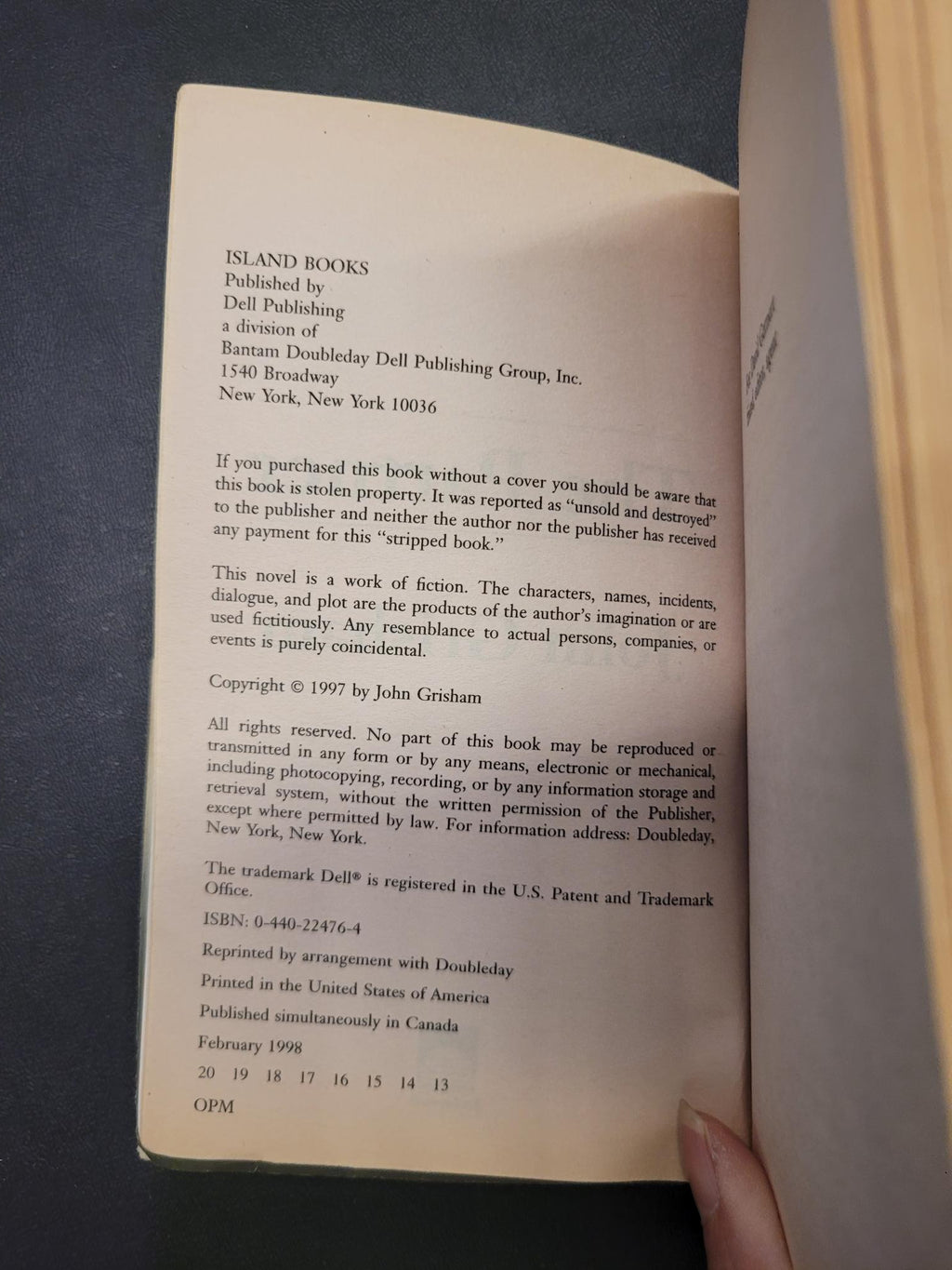 A close-up of an open book showing the copyright page on the left and a hand holding the right page. The page has black text on aged cream paper, and a wooden book spine is visible at the top.