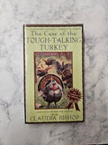 The book cover of 'The Case of the Tough-Talking Turkey' by Claudia Bishop, featuring a light green background and an illustration of a turkey, placed on a white and gray marble surface.