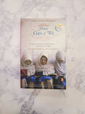 The book 'Three Cups of Tea' by Poul Nørgaard lies flat on a white and gray marble-patterned surface. The cover features a photograph of three women in white hijabs and displays the Penguin logo in the top right corner.